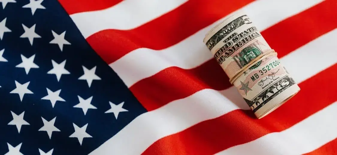 American flag with a rolled up bundle of cash laying on top of it.